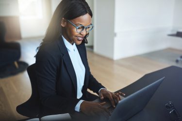 Smiling young African American businesswoman working online with a laptop at her desk in a bright modern office